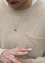 a solid 14k gold necklace with a heart pendant and a ring, against a beige sweater background from the sparkle bar