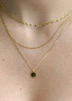 Sb Studio 14k yellow gold Love Token charm pendant layered with delicate gold chains on a woman's neck.