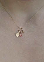sb studio gold pendant necklace featuring a small engravable charm, a pink gemstone, and a tiny star charm.