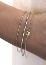 The Sparkle Bar 14k yellow gold butterfly charm bracelet worn on a wrist alongside two delicate diamond tennis bracelets.