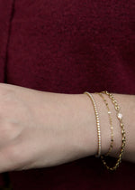 solid 14k Gold bracelets on a wrist against a maroon background from SB Studio formerly the Sparkle Bar in edmonton