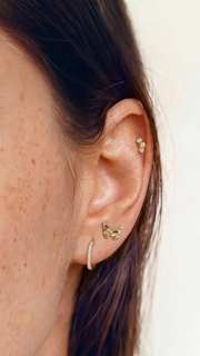 SB Studio Cecilia huggie hoop earrings in 14k gold with white topaz, worn on a model's ear with other jewelry.