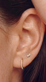 SB Studio Cecilia huggie hoop earrings in 14k gold with prong-set white topaz worn on a model's earlobe.