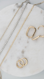 SB Studio Cecilia huggie hoop earrings in 14k yellow gold with white topaz, displayed on a marble surface.