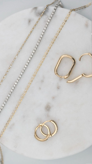 SB Studio Cecilia huggie hoop earrings in 14k yellow gold with white topaz, displayed on a marble surface.