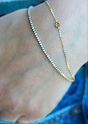 Sb Studio 14k yellow gold button charm bracelet layered with a delicate diamond tennis bracelet on a wrist