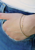 Sb Studio 14k yellow gold button charm bracelet layered with a diamond tennis bracelet on a wrist