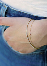 Sb Studio 14k yellow gold button charm bracelet layered with a diamond tennis bracelet on a wrist