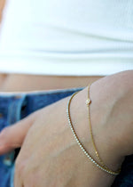 Sb Studio 14k yellow gold button charm bracelet layered with a delicate diamond tennis bracelet on a wrist.