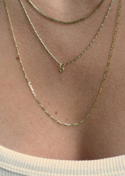 Sb Studio 14k yellow gold button charm pendant worn on a delicate layered cable chain necklace.