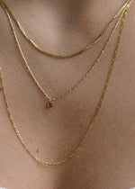 Sb Studio 14k yellow gold button charm pendant on a delicate layered gold chain necklace worn on a neck.