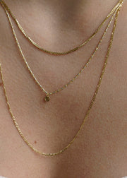 Sb Studio 14k yellow gold button charm pendant on a delicate layered gold chain necklace worn on a neck.