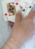 Sb Studio Mon Petit Coeur charm bracelet in 14k yellow gold with white topaz, worn layered on a wrist.
