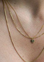 SB Studio 14k yellow gold heart charm pendant on a delicate layered gold chain necklace worn on a person.