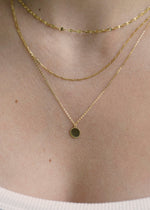 Sb studio 14k yellow gold Love Token charm pendant layered on delicate gold chains around a woman's neck.