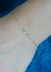 Sb Studio 14k yellow gold cable chain bracelet featuring a delicate bezel-set heart-shaped opal charm on wrist.