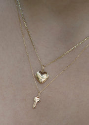 Two gold necklaces with heart and key pendants on a woman