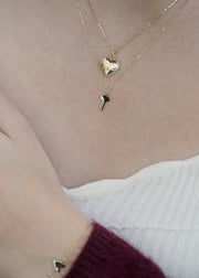 Close-up of two solid1 4k gold necklaces with heart and key pendants on a neutral background from sb studio