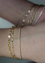 Close-up of a wrist wearing multiple solid 14k gold bracelets on a neutral background