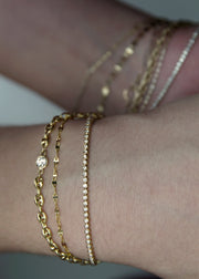 Close-up of a wrist wearing multiple solid 14k gold bracelets on a neutral background