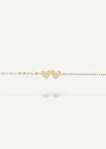 Gold bracelet with two heart-shaped charms on a white background