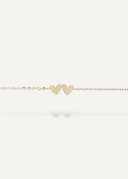 Gold bracelet with two heart-shaped charms on a white background