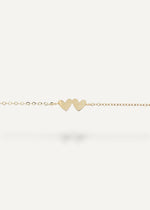 Gold bracelet with two heart-shaped charms on a white background