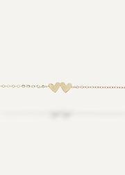 Gold bracelet with two heart-shaped charms on a white background
