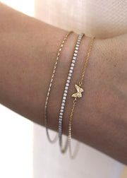 The Sparkle Bar 14k yellow gold butterfly charm bracelet worn on a wrist alongside two delicate diamond tennis bracelets.