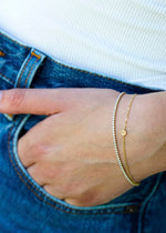 The Sparkle Bar Cute As A Button charm bracelet in 14k yellow gold worn with a diamond tennis bracelet on a wrist.